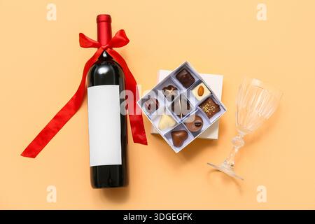 Köstliche Schokoladenbonbons in Box, Flasche Wein und Glas auf orangem Hintergrund Stockfoto