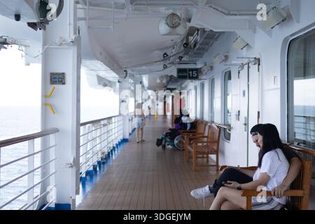 Lange Holzstege erstrecken sich über das Außendeck eines Kreuzfahrtschiffs, mit Meeresbrise und offenem Meerblick, die eine entspannte Atmosphäre an Bord schaffen. Stockfoto