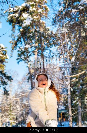 Fröhliche Frau in warmen Kleidern, die im Winter draußen Schnee wirft. Stockfoto