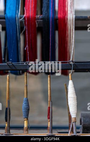 Bunte Garnspulen auf Holzspindeln sind bereit für den Einsatz auf einem antiken Textilwebstuhl, der traditionelles Handwerk, Faserkunst und die Geschichte von repräsentiert Stockfoto