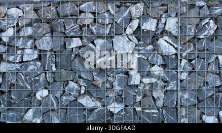 Gitterrahmen der Erdrutschschutzkonstruktion aus Eisenkäfig gefüllt mit rauen grauen Natursteinen, feste industrielle Textur grafische Ressource Stockfoto