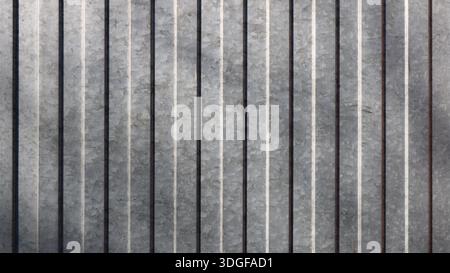 Verzinktes Metallblech mit einer silbernen geprägten Oberfläche mit vertikalen konvexen Streifen, grauem strukturiertem Eisenhintergrund, Fragment eines Zauns Stockfoto