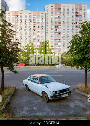 Kiew, Ukraine - 27. Juni 2025: Ein verlassener weißer Toyota Carina aus den 1980er Jahren parkte in der Revutsky Straße, mit hohen Wohngebäuden bedeckt mit gr Stockfoto