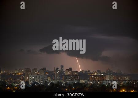 Ein starker Blitz blitzt über den dunklen, stürmischen Himmel während eines nächtlichen Gewitters im Sommer. Unterhalb der beleuchteten Skyline von Kiew, Ukraine, Stockfoto