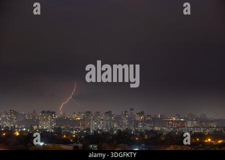 Ein starker Blitz blitzt über den dunklen, stürmischen Himmel während eines nächtlichen Gewitters im Sommer. Unterhalb der beleuchteten Skyline von Kiew, Ukraine, Stockfoto