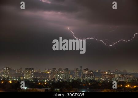 Ein starker Blitz blitzt über den dunklen, stürmischen Himmel während eines nächtlichen Gewitters im Sommer. Unterhalb der beleuchteten Skyline von Kiew, Ukraine, Stockfoto