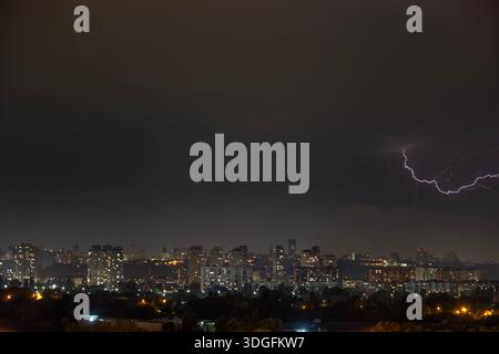 Ein starker Blitz blitzt über den dunklen, stürmischen Himmel während eines nächtlichen Gewitters im Sommer. Unterhalb der beleuchteten Skyline von Kiew, Ukraine, Stockfoto