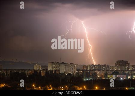 Ein starker Blitz blitzt über den dunklen, stürmischen Himmel während eines nächtlichen Gewitters im Sommer. Unterhalb der beleuchteten Skyline von Kiew, Ukraine, Stockfoto