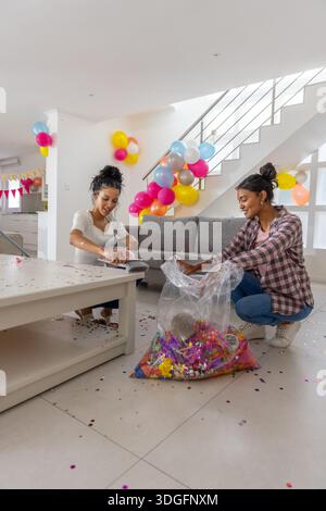 Diverse Mutter und Teenager-Tochter knieten auf gefliestem Wohnzimmerboden und hüpften Konfetti Stockfoto