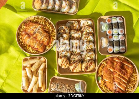 Flache Auswahl an asiatischen Gerichten zum Mitnehmen, darunter Sushi-Brötchen, frittierte Snacks und Hühnchennudelschüsseln. Ein lebendiger Mix aus Texturen, ideal für die Straße Stockfoto