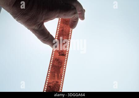Eine Hand hält einen Streifen Schwarzweiß-Film vor einem hellen Hintergrund und zeigt Bilder von Bäumen und einem Gebäude. Nostalgie nach alter Technik Stockfoto