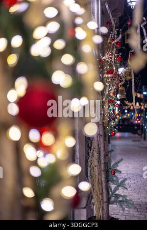 Vertikale Nachtansicht auf Weihnachtsdekorationen mit roten Ornamenten und warmweißen Lichtern mit schwerem Bokeh aus einer verschwommenen Stadtstraße und Autolichtern Stockfoto