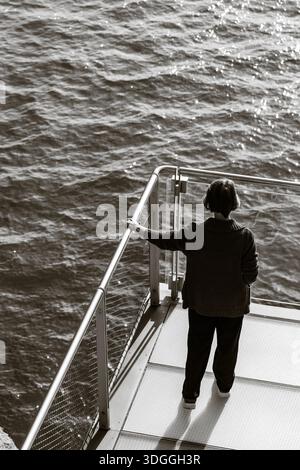 Santander, Spanien – 20. November 2021: Schwarzweißaufnahme einer Frau, die auf dem Metalldeck des Centro Botin steht und auf die strukturierte Wa hinunterblickt Stockfoto