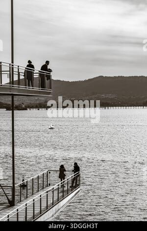 Santander, Spanien – 20. November 2021: Kontrastreiches Schwarz-weiß-Foto von Silhouetten von Menschen auf dem Metalldeck des Centro Botin gegen den hellen Shi Stockfoto