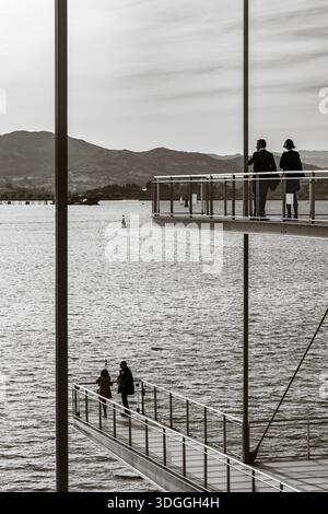 Santander, Spanien – 20. November 2021: Vertikale schwarz-weiße Aufnahme von Silhouetten von Menschen auf dem auskragenden Deck, eingerahmt von den strukturellen Säulen von C Stockfoto
