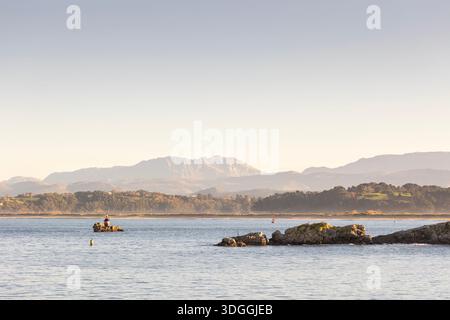Ein malerischer Blick auf die felsige Insel Isla Horadada in der Bucht von Santander, Spanien, mit trüben Bergen im Hintergrund an einem sonnigen Tag. Stockfoto