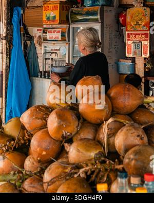 Straßenverkäuferin, die kalte Kokosnussgetränke auf dem Vietnammarkt zubereitet Stockfoto