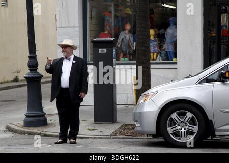 Ein älterer Mann in formeller Kleidung steht vor einem Schaufenster an einer Straßenecke. Ein modernes Auto parkt nebenan, Savannah, Georgia, USA Stockfoto