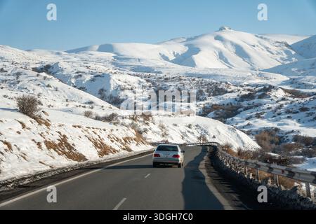 Armenien - 8. Januar 2026: Auto fährt auf einer offenen Bergstraße durch schneebedeckte Hügel und weite Täler bei klarem Wintertag Stockfoto