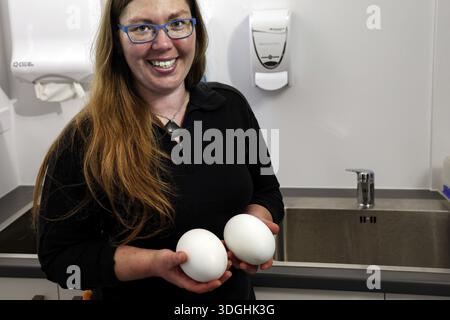 Frau lächelt, während sie zwei Kiwieier in der Hand hält, Rotorua, Bay of Plenty, Neuseeland Stockfoto