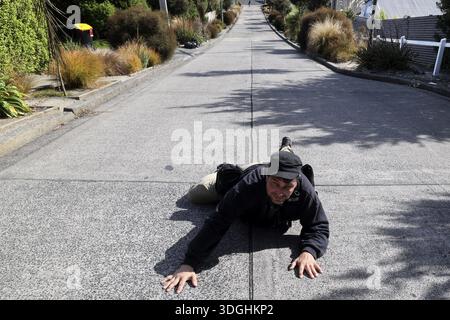 Eine Person liegt humorvoll auf der steilen Baldwin Street in Dunedin, Dunedin, Zero, Neuseeland Stockfoto