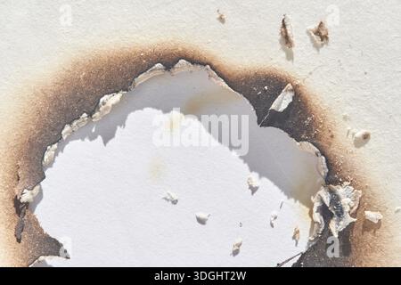 Verbranntes Papier mit unregelmäßigen Brandspuren auf weißer Oberfläche, die Schäden und Textur zeigen. Stockfoto