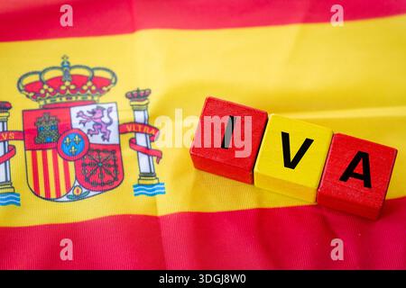 Das Wort IVA (spanische Mehrwertsteuer) steht in Rot auf gelben Würfeln. Die Flagge Spaniens im Hintergrund. Finanz- und Geschäftskonzept. Nahaufnahme Stockfoto