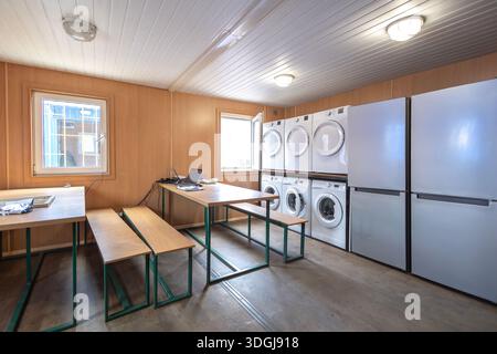 Eine geräumige, gemeinschaftliche Kantine in einer modularen Kabine, ausgestattet für verschiedene Bedürfnisse von Zeitarbeitern. Die All-in-One-Einrichtung umfasst Esstische, Stockfoto