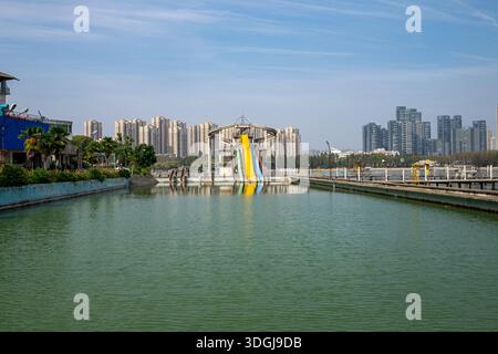 Eine Landschaftsaufnahme eines vernachlässigten Schwimmbades, gefüllt mit grünem, stehendem Wasser. Im Hintergrund, farbenfrohe Wasserrutschen und moderne Stadtwohnung B Stockfoto
