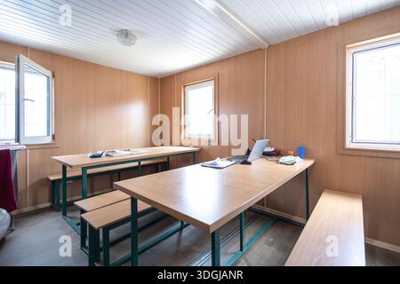 Eine Arbeitskantine in einer modularen Kabine mit langen Tischen und Sitzbänken für Mahlzeiten. Ein Laptop schlägt vor, dass der Platz auch für Pausen oder Arbeiten während der Zeit genutzt wird Stockfoto