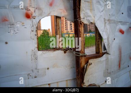 WUHAN, CHINA - 24. JULI 2016: Ein Blick durch ein zerklüftetes Loch, das in einem weißen Bauwerk zerrissen wurde, zeigt die verlassene Stelle und den Bau Stockfoto