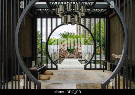 HANGZHOU, CHINA - 03. JULI 2017: Blick vom Inneren eines modernen Pavillons im chinesischen Stil mit Blick durch große kreisförmige Rahmen. Niedrige Tische mit Teesets Stockfoto