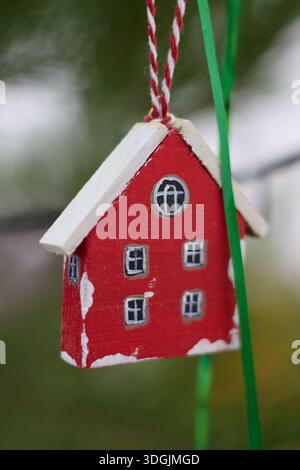 Dieses Bild zeigt ein bezauberndes rotes Holzspielhaus-Weihnachtsschmuck, kunstvoll mit einem weißen Dach und bemalten Details. Das Miniaturhaus Stockfoto