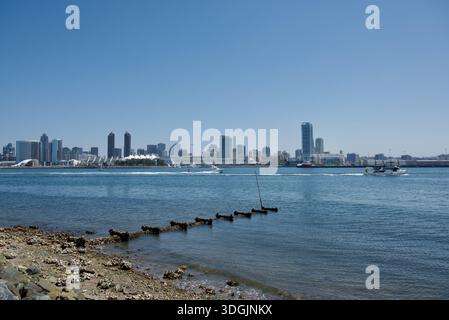 Blick auf die San Diego Bay und die Innenstadt von San Diego von Coronado. Felsige Küste mit Trümmern und Algen, ruhiges Wasser mit Booten und die Skyline. Stockfoto