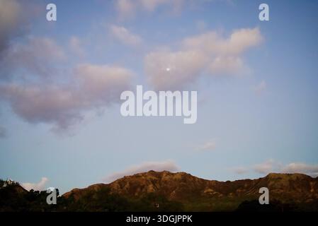 Ein großer Mond scheint durch die Wolken über den sanften Hügeln von Diamond Head und begrüßt Besucher am frühen Morgen im atemberaubenden Naturpark. Stockfoto