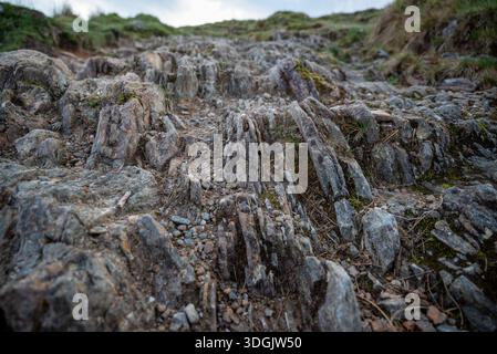 Eine detaillierte Aufnahme gezackter, vertikaler Felsschichten und strukturierter Steinschichten auf einem Bergwanderweg auf Ben Lomond in Schottland. Stockfoto