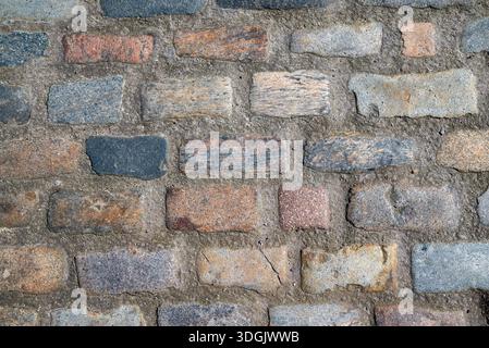 Überkopfaufnahme aus mehrfarbigem Granit-Kopfsteinpflaster in Mörtel, perfekt für architektonische oder Hintergrundanwendungen. Stockfoto