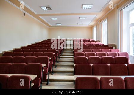 Weitwinkelansicht eines leeren Universitätsvorlesungssaals. Reihen kastanienbrauner Sitze mit kleinen Holzschreibtischen blicken auf die Vorderseite des Auditoriums, der ha ist Stockfoto