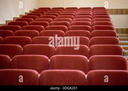 Eine Nahaufnahme der leeren kastanienbraunen Sitze in einem Universitätsvorlesungssaal. Die weichen, gepolsterten Stühle sind in ordentlichen Reihen mit Holz angeordnet Stockfoto