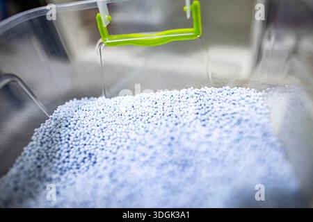 Eine Makroaufnahme hellblauer Kunststoffgranulate. Diese Polymergranulate sind ein Rohstoff für die industrielle Fertigung und werden in einem großen, transparenten Gehäuse gelagert Stockfoto
