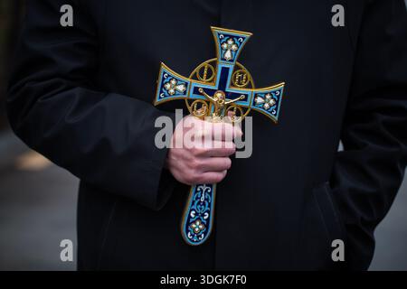 Nahaufnahme eines Mannes, der während eines traditionellen relig ein großes, reich verziertes goldenes Kreuz mit blauer Emailverzierung vor schwarzem Fellhintergrund hält Stockfoto