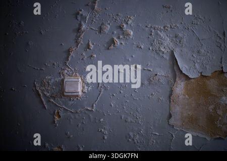 Alte, verwitterte blaue Wandoberfläche mit abblätternder Farbe und ein Vintage-Lichtschalter in einem dunklen, verlassenen Hauszimmer erzeugen ein gruseliges, geheimnisvolles Grinsen Stockfoto