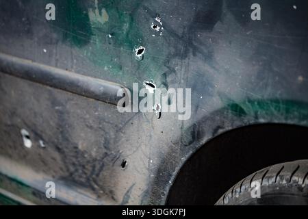 Detailansicht eines gezackten Schrapnell-Lochs in der schmutzigen, zerkratzten grünen Metalltür eines Mühlenfahrzeugs, das durch schwere Artillerie oder Mörserbeschuss beschädigt wurde Stockfoto
