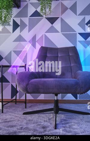 Grauer Sessel mit violetten und blauen Neonlichtern und gemusterten geometrischen Tapeten Stockfoto