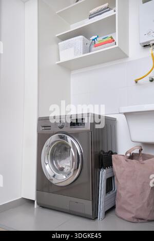 Waschraum mit Waschmaschine, organisierten Regalen und einer Wäschetasche Stockfoto