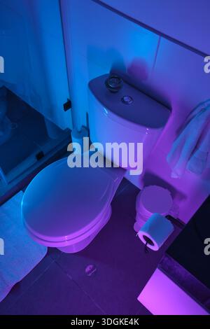 Die Innenausstattung des Badezimmers ist mit einer Toilette in leuchtendem Blau und Lila und stimmungsvoller Beleuchtung ausgestattet Stockfoto