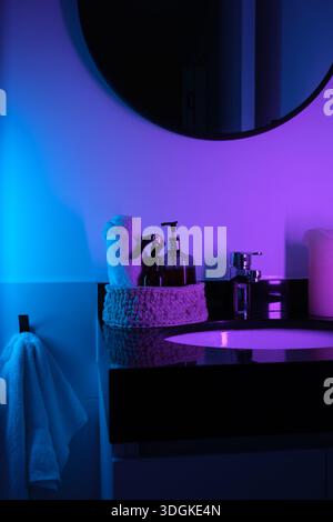 Modernes Badezimmer mit Waschbecken und Spiegel, die in leuchtenden Neontönen beleuchtet sind Stockfoto