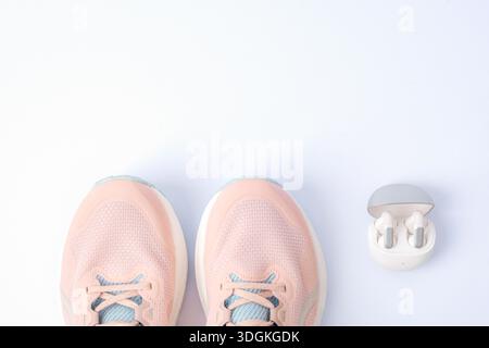 Sportschuhe und schnurlose Ohrstöpsel auf weißem Hintergrund mit Kopierraum darüber. Draufsicht, flach. Stockfoto