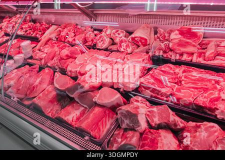 Gekühltes frisches Fleisch mit roter Beleuchtung. Frische Rindfleisch- und Schweinefleisch werden in einer Fleischvitrine in einem lokalen Geschäft organisiert. Das leuchtende Rot Stockfoto