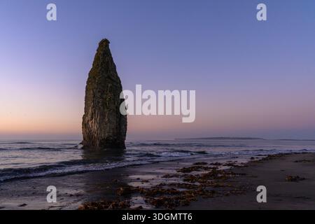 Eine atemberaubende Felsformation erhebt sich eindrucksvoll aus dem ruhigen Meer, während die Dämmerung an einem ruhigen russischen Strand absinkt. Sanfte Wellen schlagen sanft gegen den Sand Stockfoto